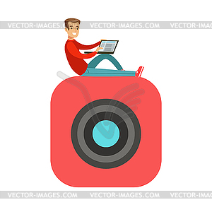 Young smiling man sitting on big mobile app symbol - vector clipart
